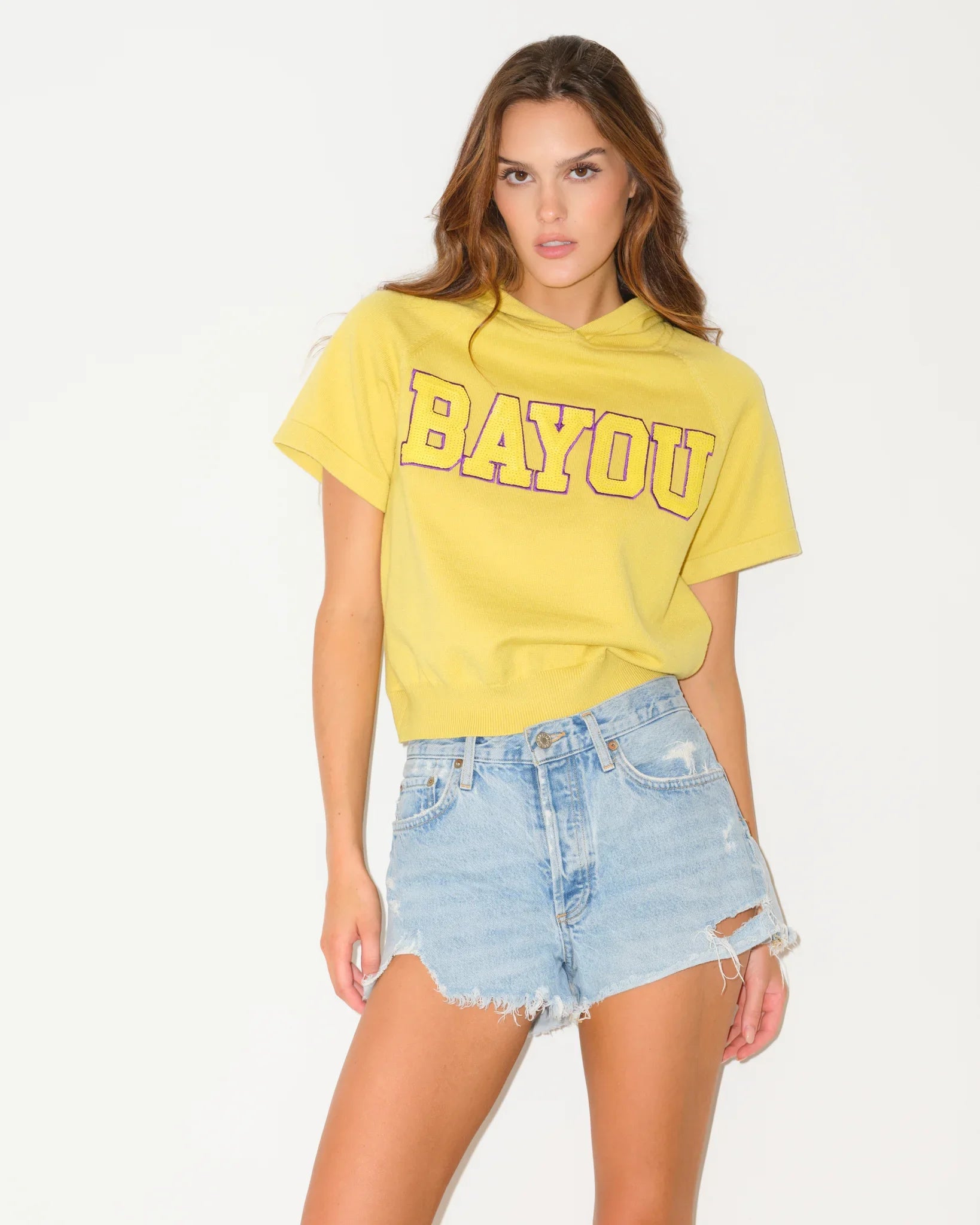 Yellow short sleeve cropped hoodie with bold "BAYOU" varsity lettering across the chest, featuring subtle sequin texture throughout the knit fabric.