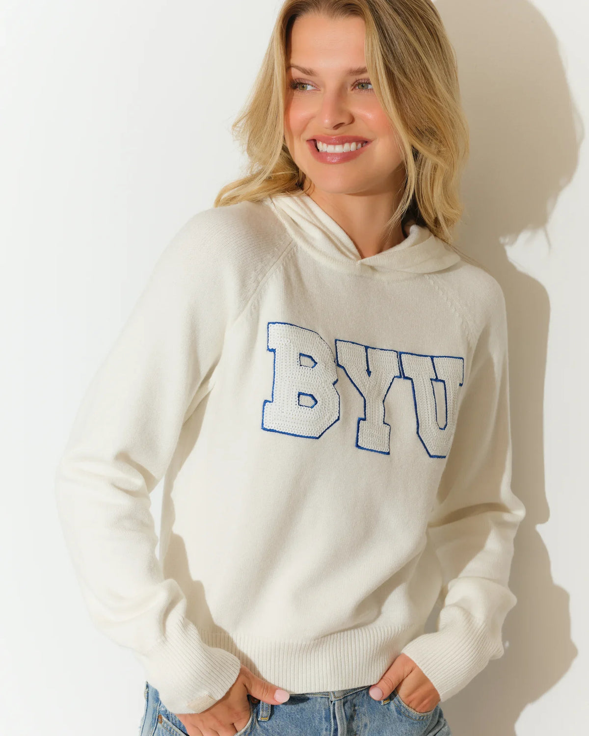 White BYU Cougars sequin knit hoodie featuring bold blue sequined "BYU" lettering across the chest, with a relaxed cropped fit and kangaroo hood.