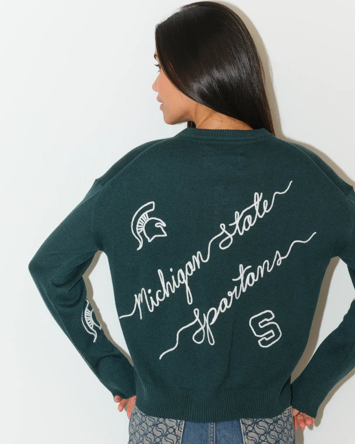 Evergreen Michigan State Spartans crew neck sweater with cursive script lettering and Spartan logo on the sleeve, paired with jeans.