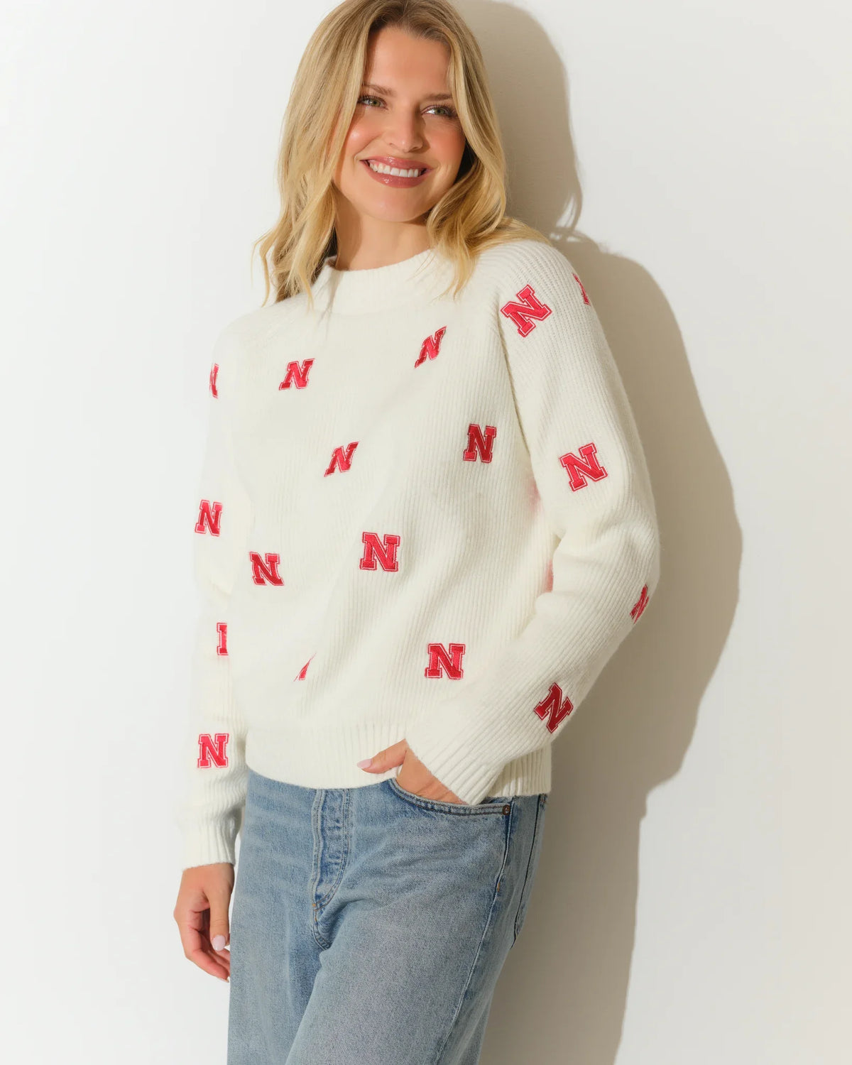 Ivory Nebraska Cornhuskers fisherman sweater with allover red "N" logo pattern, crew neck, and long sleeves, styled with jeans.