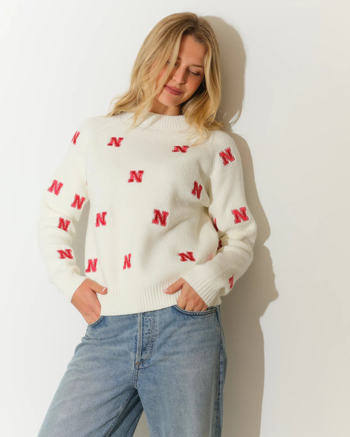 Ivory Nebraska Cornhuskers fisherman sweater with allover red "N" logo pattern, crew neck, and long sleeves, styled with jeans.