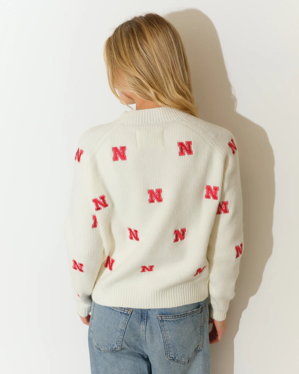 Ivory Nebraska Cornhuskers fisherman sweater with allover red "N" logo pattern, crew neck, and long sleeves, styled with jeans.