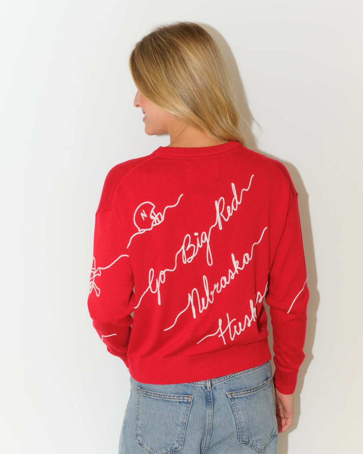 Red Nebraska Cornhuskers women's crewneck sweater with white cursive script reading "Big Red," "Nebraska," and "Huskers" across the front and sleeves.