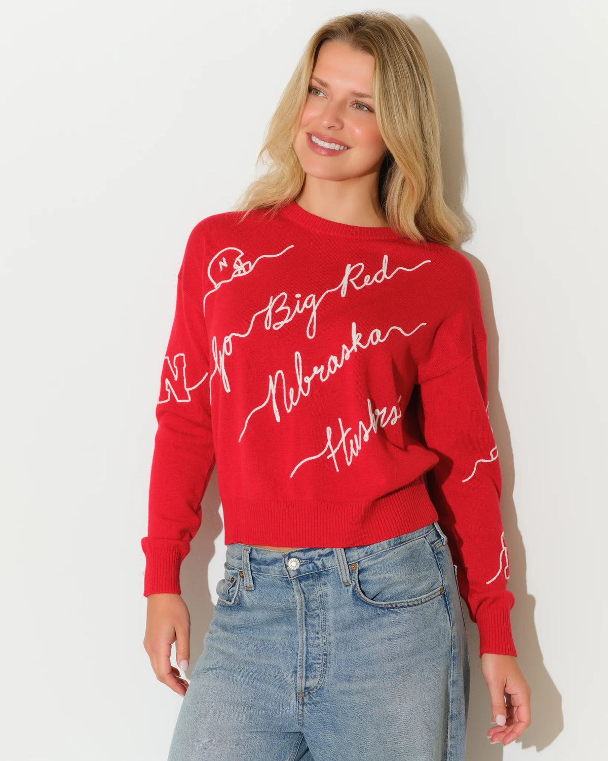 Red Nebraska Cornhuskers women's crewneck sweater with white cursive script reading "Big Red," "Nebraska," and "Huskers" across the front and sleeves.