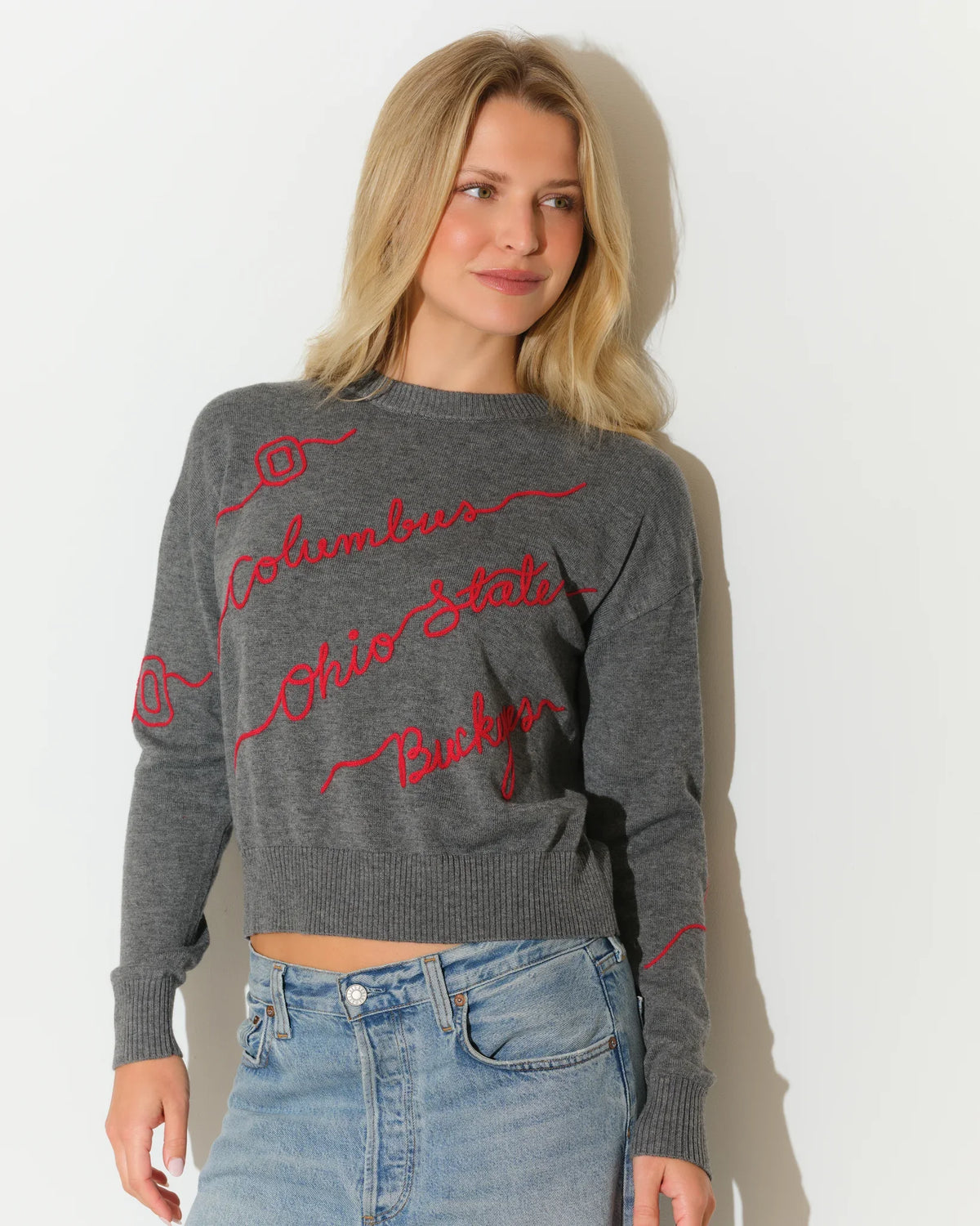 Gray Ohio State Buckeyes cropped knit sweater with red cursive script lettering across the front, styled with light wash denim.