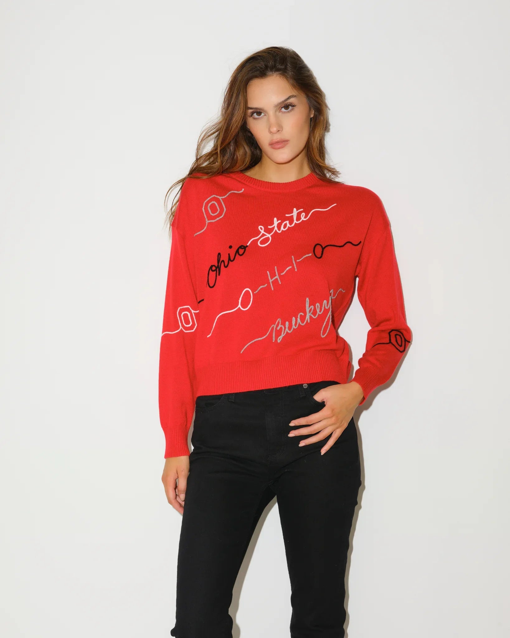 Red Ohio State Buckeyes long-sleeve sweater with cursive script lettering across the chest, styled with black flare pants.