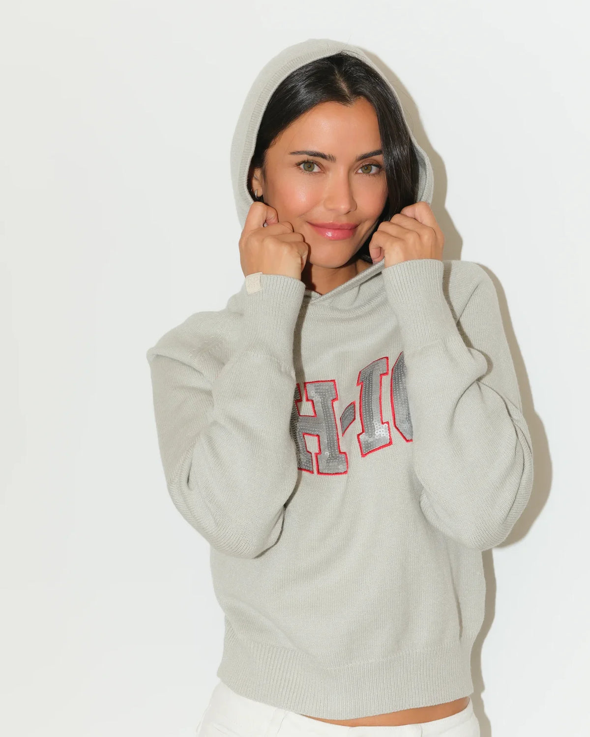 Gray Ohio State Buckeyes sequin knit hoodie with bold "OH-IO" lettering in red and gray on the chest, worn by a woman.
