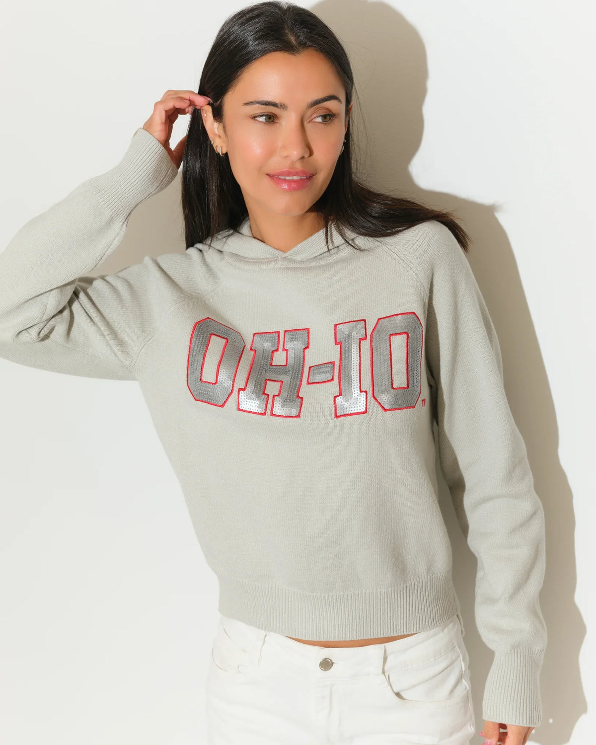 Gray Ohio State Buckeyes sequin knit hoodie with bold "OH-IO" lettering in red and gray on the chest, worn by a woman.
