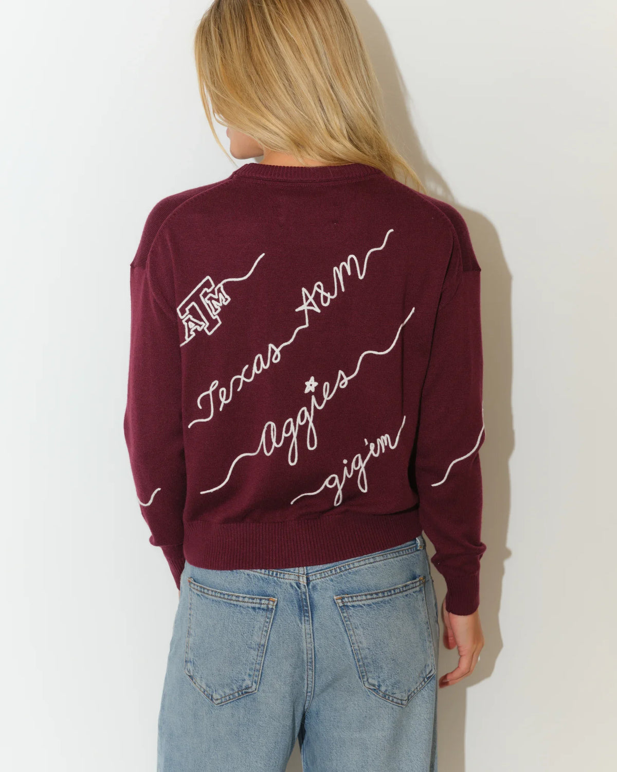 Maroon Texas A&M Aggies cropped crewneck sweater with white cursive script lettering across the front, paired with light wash jeans.