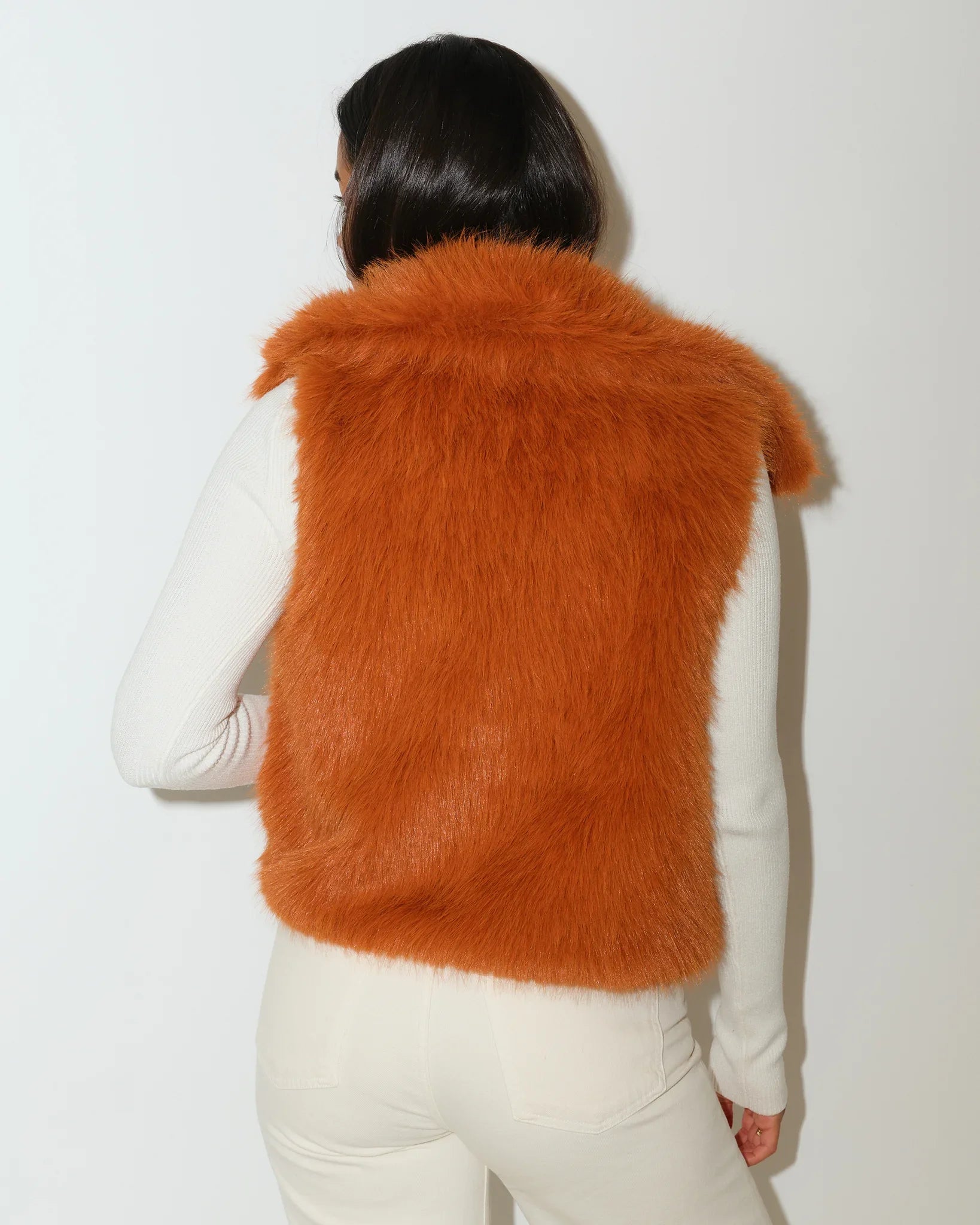 Saddle brown KADYLUXE faux fur vest with plaid lining, worn open over a white top with cream pants.