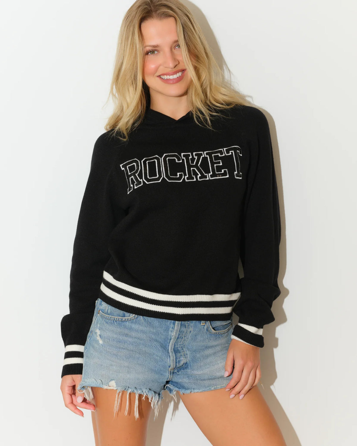 Black KADYLUXE Rocket sequin knit hoodie with bold "ROCKET" lettering and white varsity stripes at the cuffs and hem.