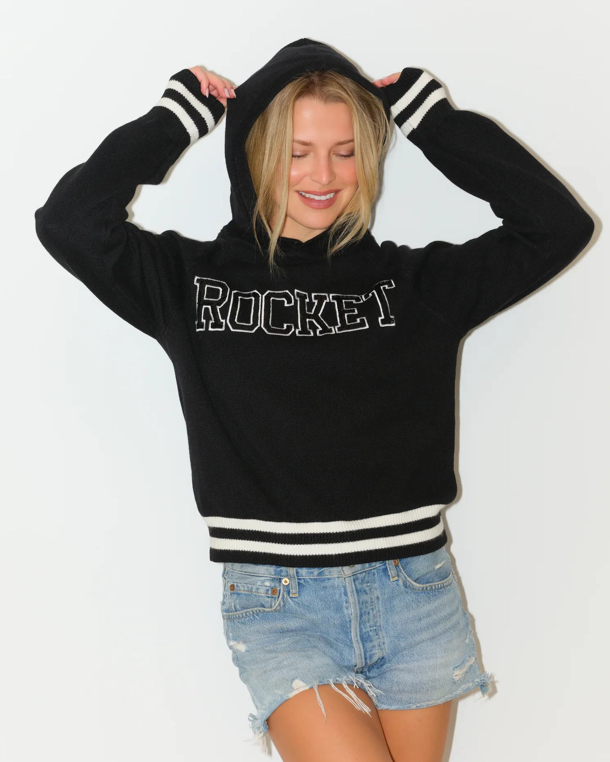 Black KADYLUXE Rocket sequin knit hoodie with bold "ROCKET" lettering and white varsity stripes at the cuffs and hem.