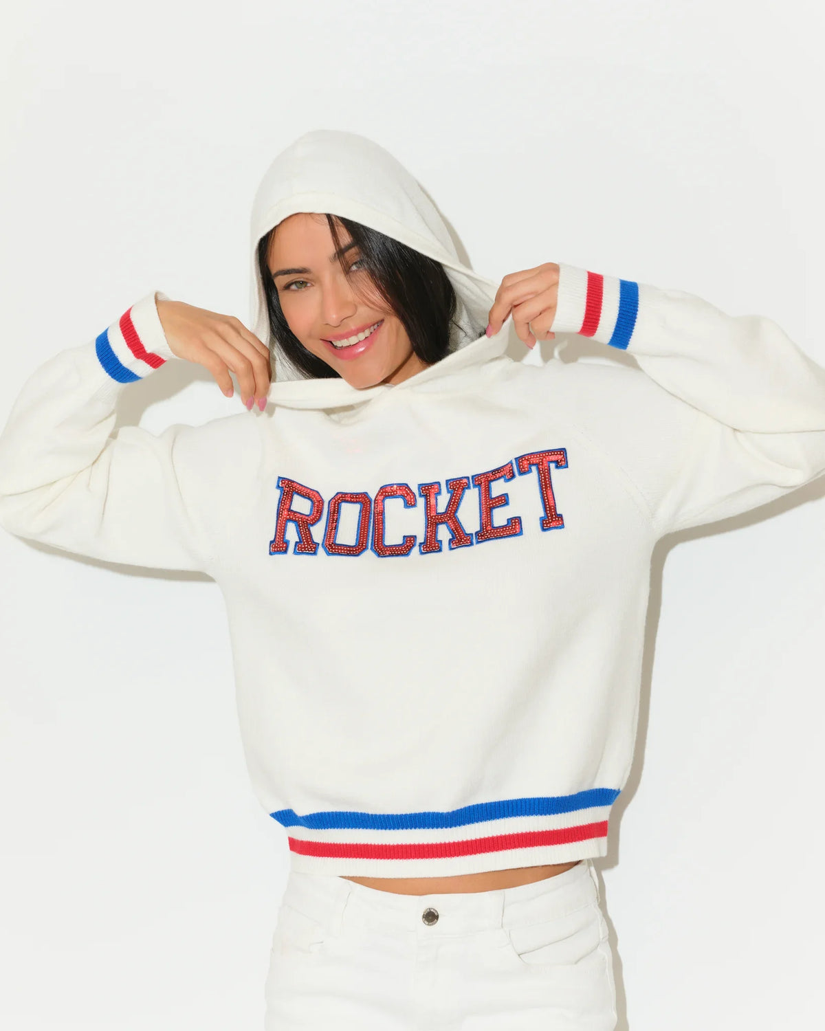 White KADYLUXE Shine Sequin Knit Hoodie with "ROCKET" in red-blue sequin letters, red and blue stripe cuffs and hem.