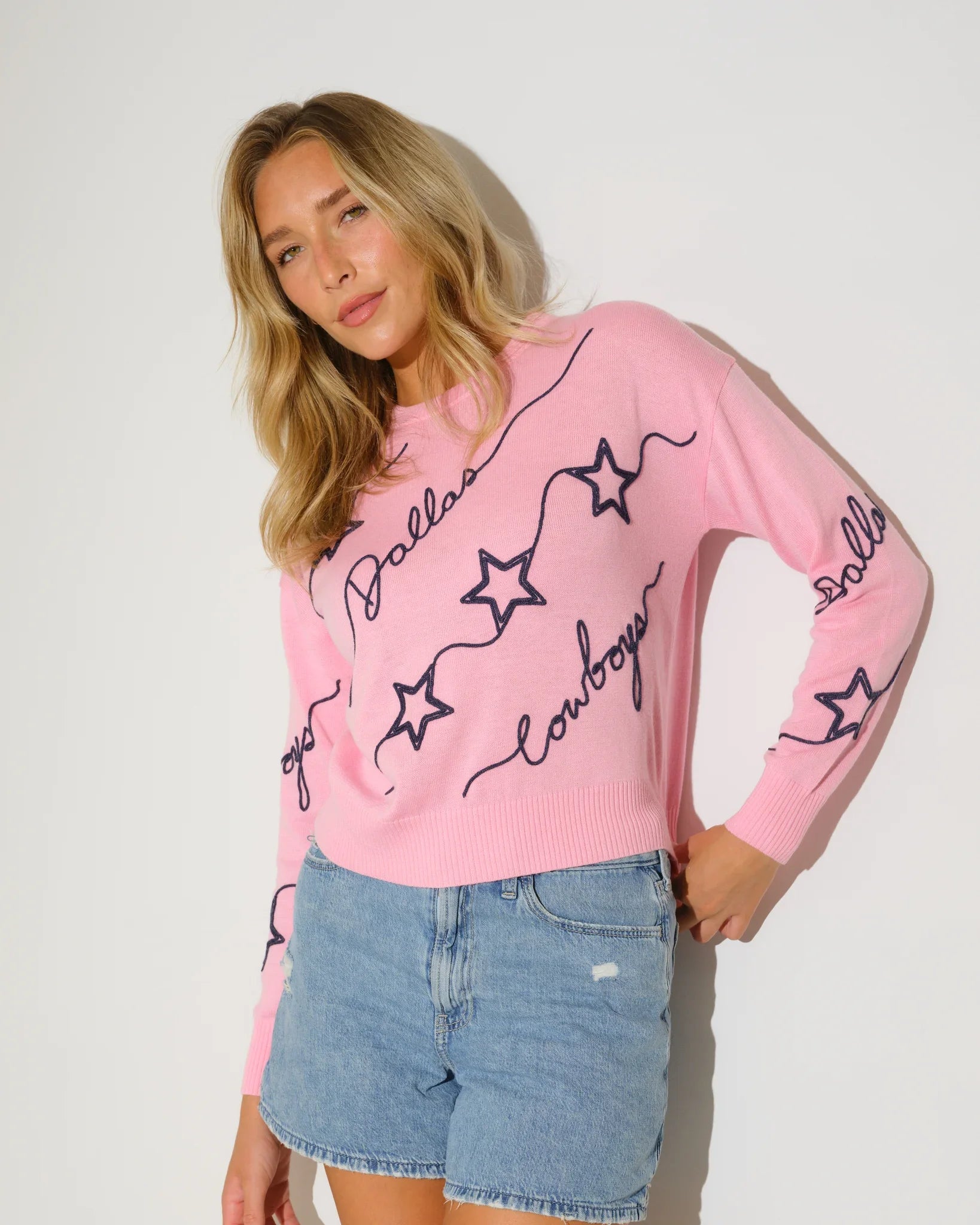 Pink Dallas Cowboys women's knit sweater with navy star pattern and script "Dallas Cowboys" lettering throughout the fabric.