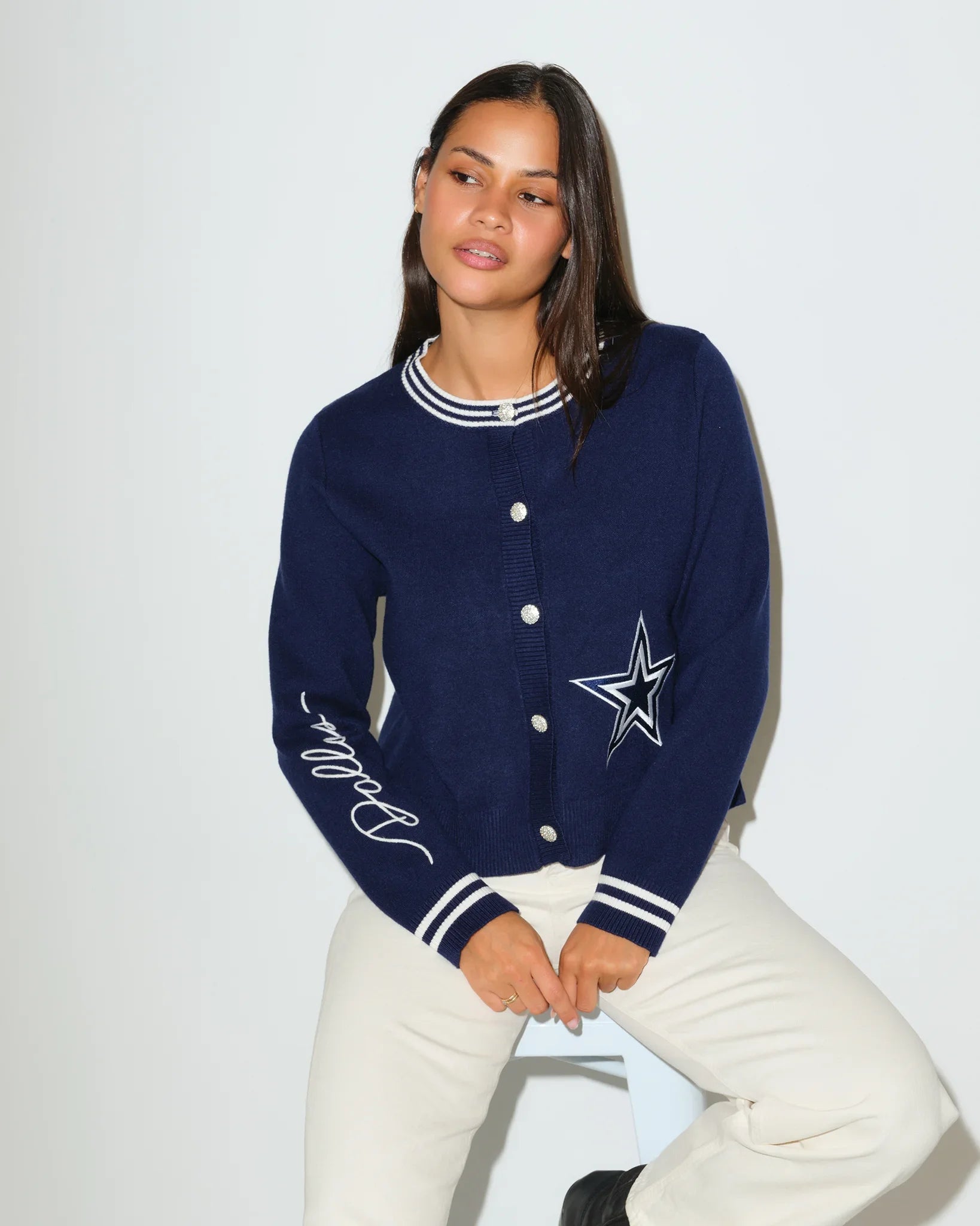 Navy Dallas Cowboys mini cardigan with silver star logo on chest, striped trim, and "Cowboys" script on sleeve, styled on a seated female model.
