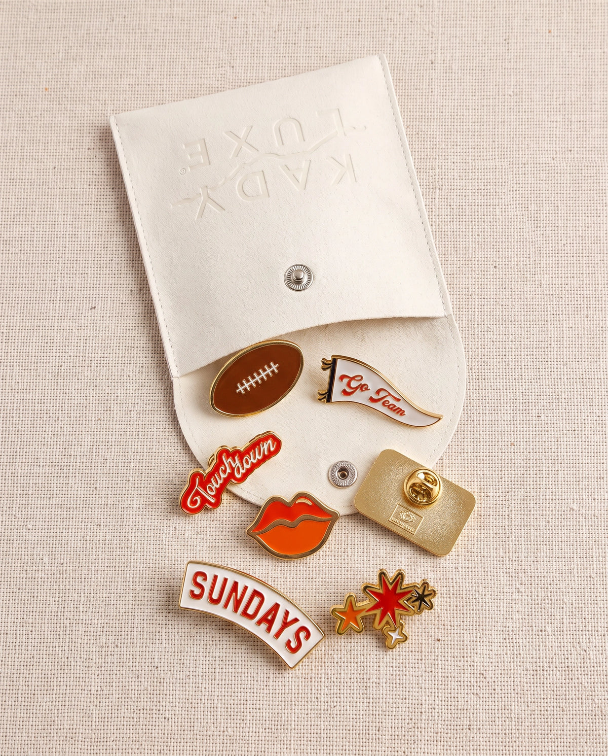 NFL Sunday themed KADYLUXE enamel pin pack in color orange. 7 pins coming out of a suede carrying pouch.