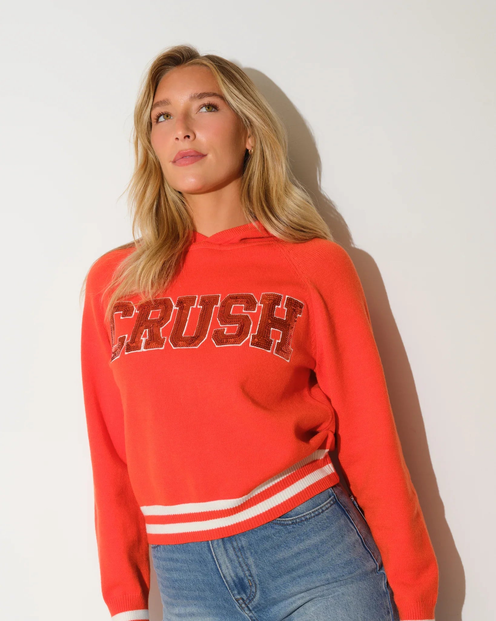 Red sequin knit hoodie with bold "CRUSH" lettering across the chest and white stripe trim at the hem.