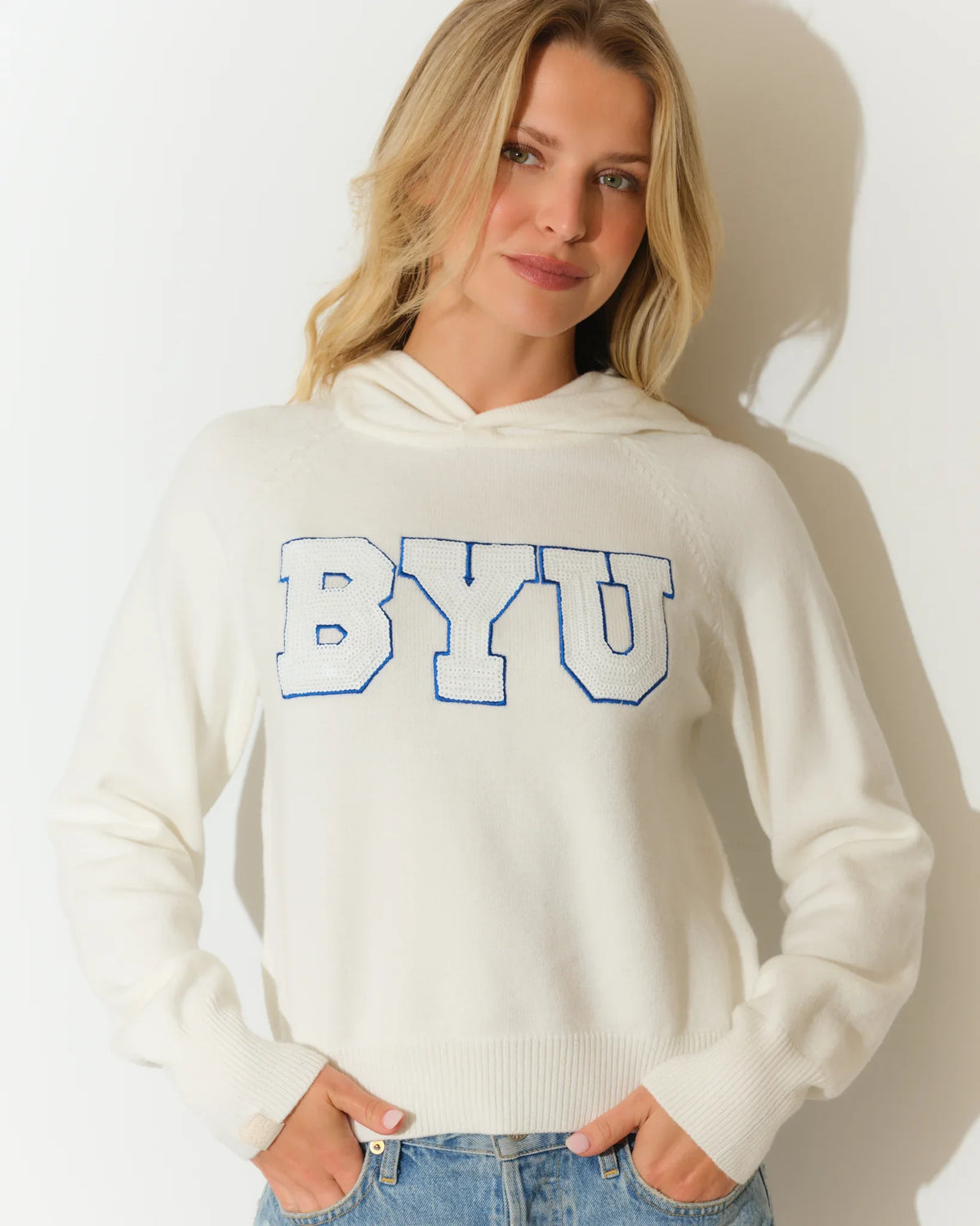 White BYU Cougars sequin knit hoodie featuring bold blue sequined "BYU" lettering across the chest, with a relaxed cropped fit and kangaroo hood.