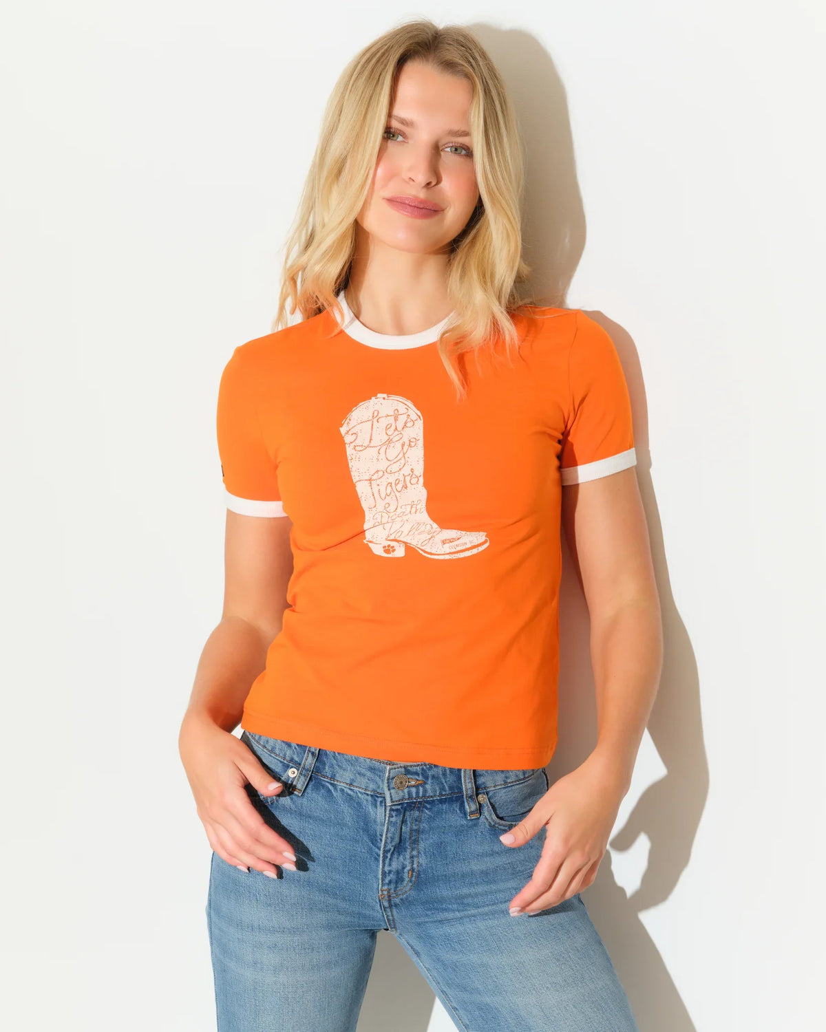 Orange Clemson Tigers women's ringer tee with white trim and a cowboy boot graphic on the chest, paired with jeans.