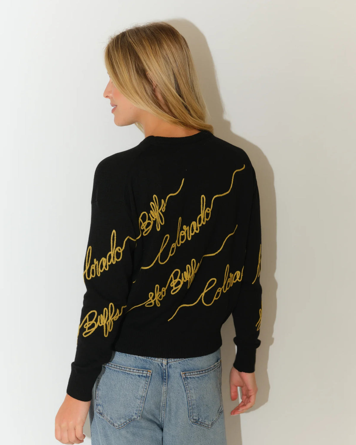 Black Colorado Buffaloes crewneck sweater with gold cursive "Colorado" script repeated across the front and sleeves.