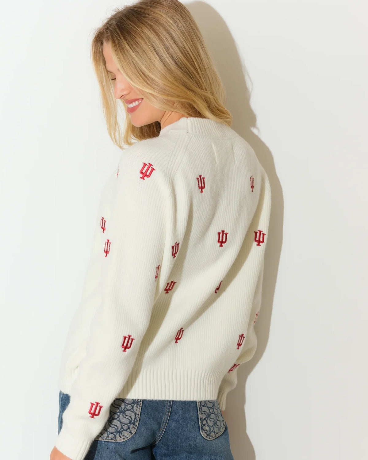 Ivory crewneck fisherman sweater featuring allover embroidered Indiana Hoosiers IU logos in red, styled with jeans.