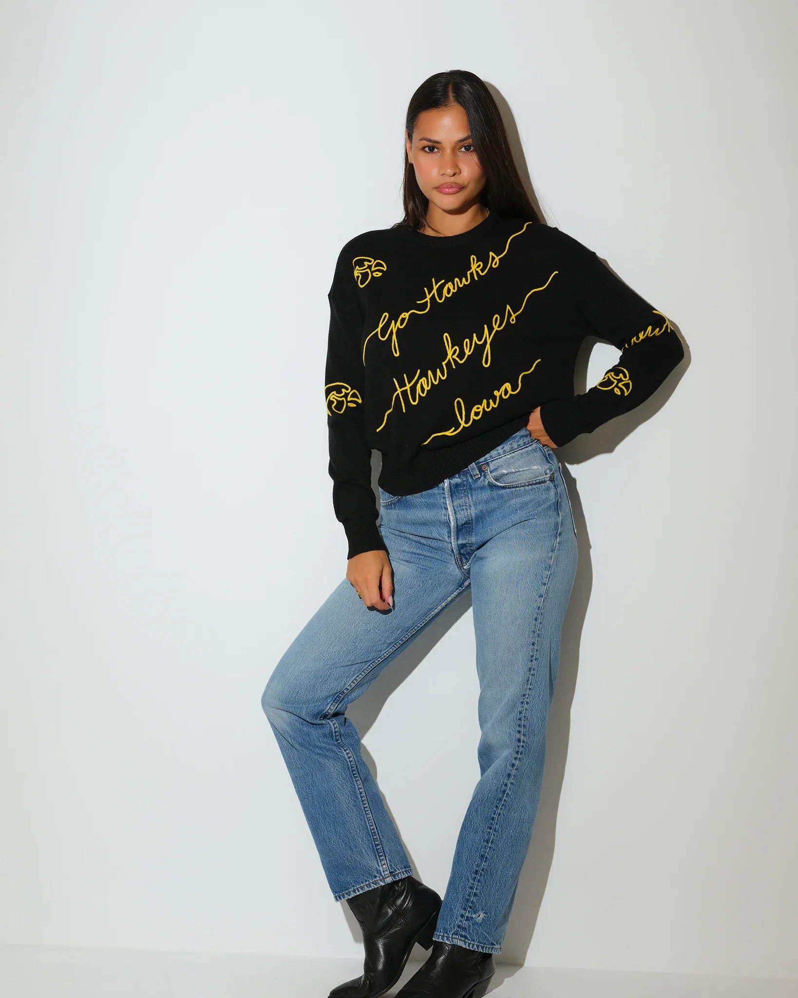 Black Iowa Hawkeyes crewneck sweater featuring gold script "Hawkeyes," "Iowa," and "Go Hawks" lettering with decorative accents throughout.