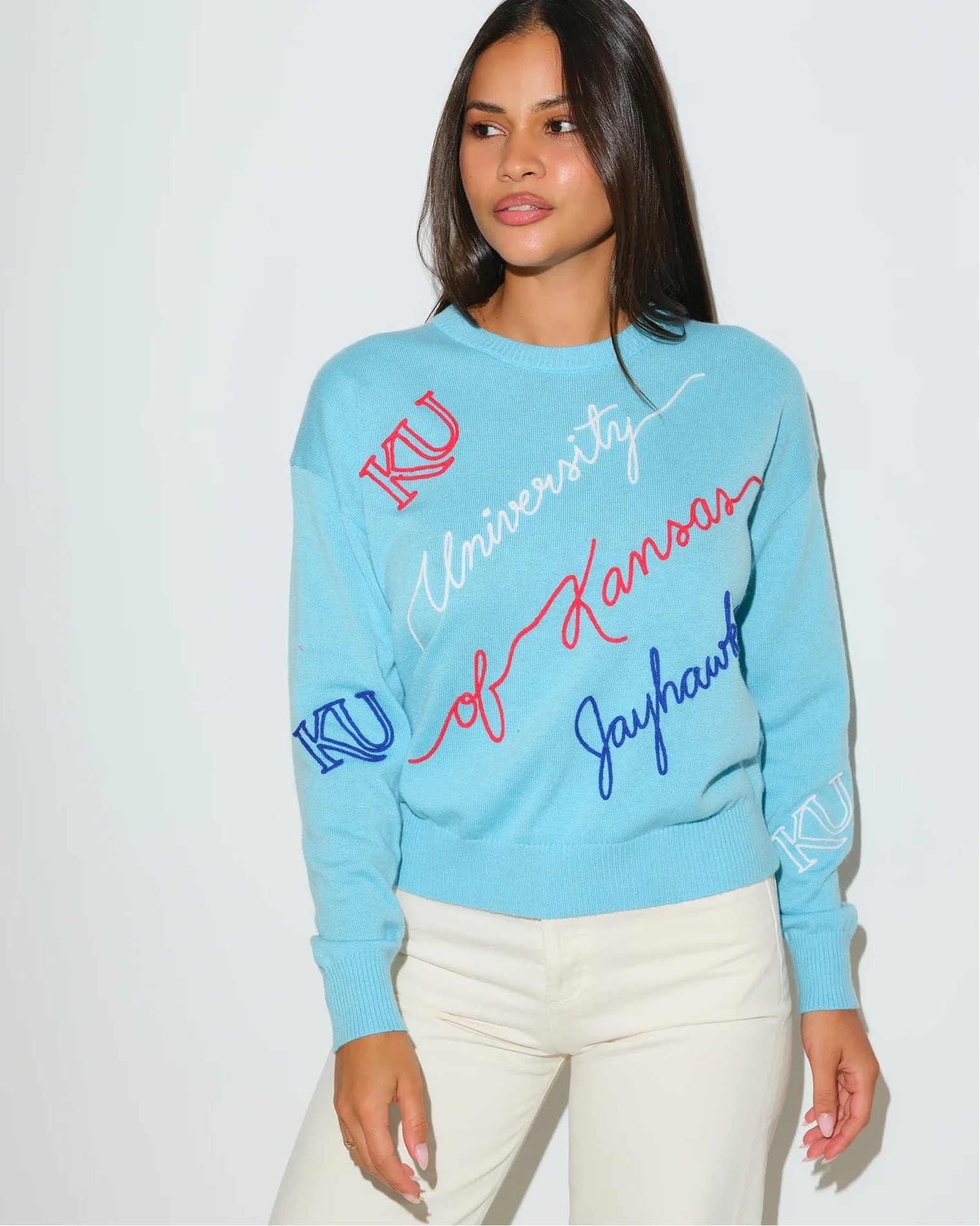 Powder blue Kansas Jayhawks crewneck sweater with cursive "University of Kansas Jayhawks" script and KU logo embroidery in red and blue.