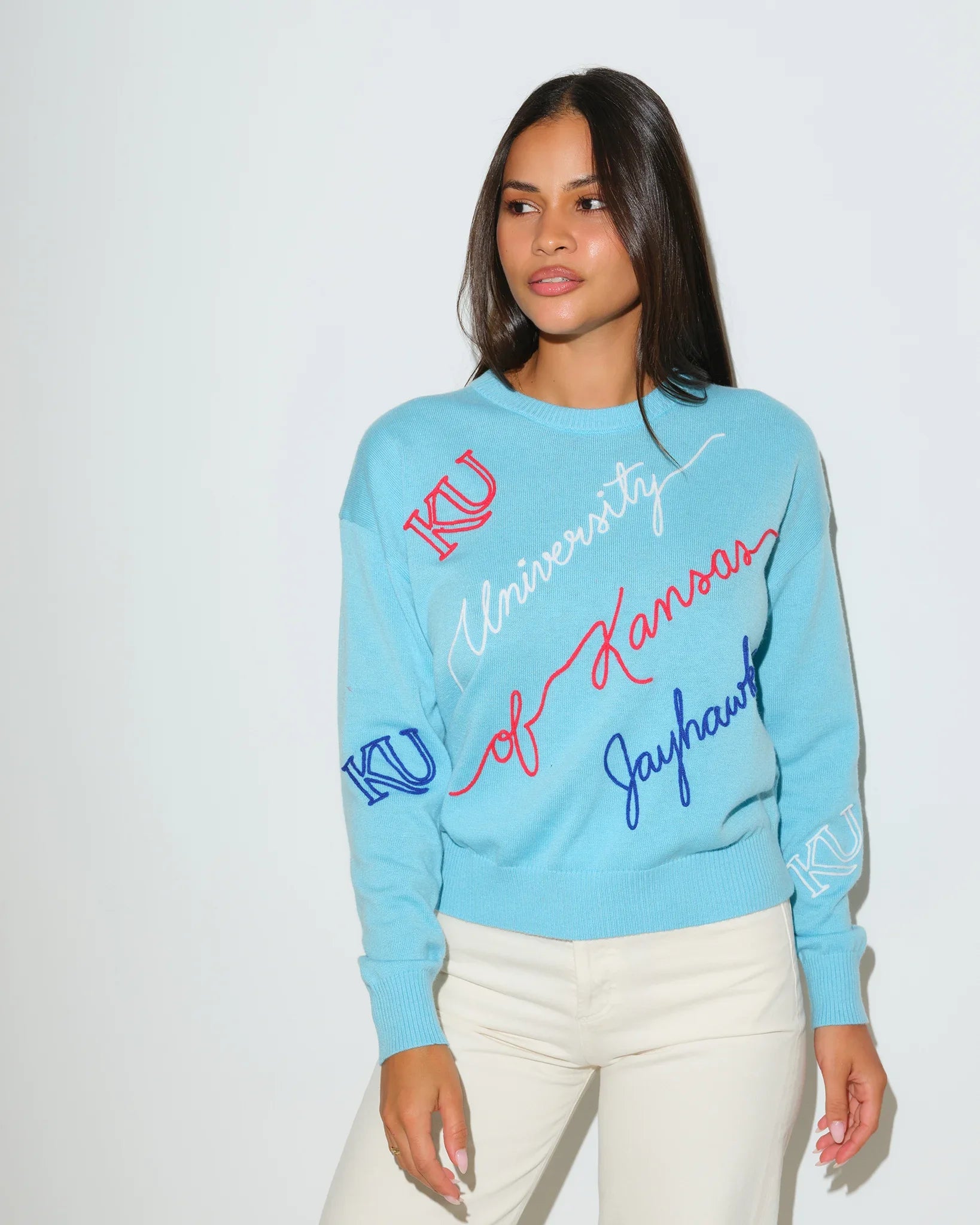 Powder blue Kansas Jayhawks crewneck sweater with cursive "University of Kansas Jayhawks" script and KU logo embroidery in red and blue.