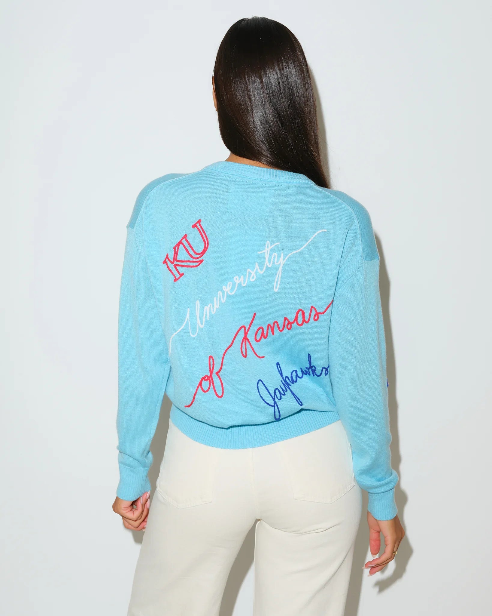 Powder blue Kansas Jayhawks crewneck sweater with cursive "University of Kansas Jayhawks" script and KU logo embroidery in red and blue.