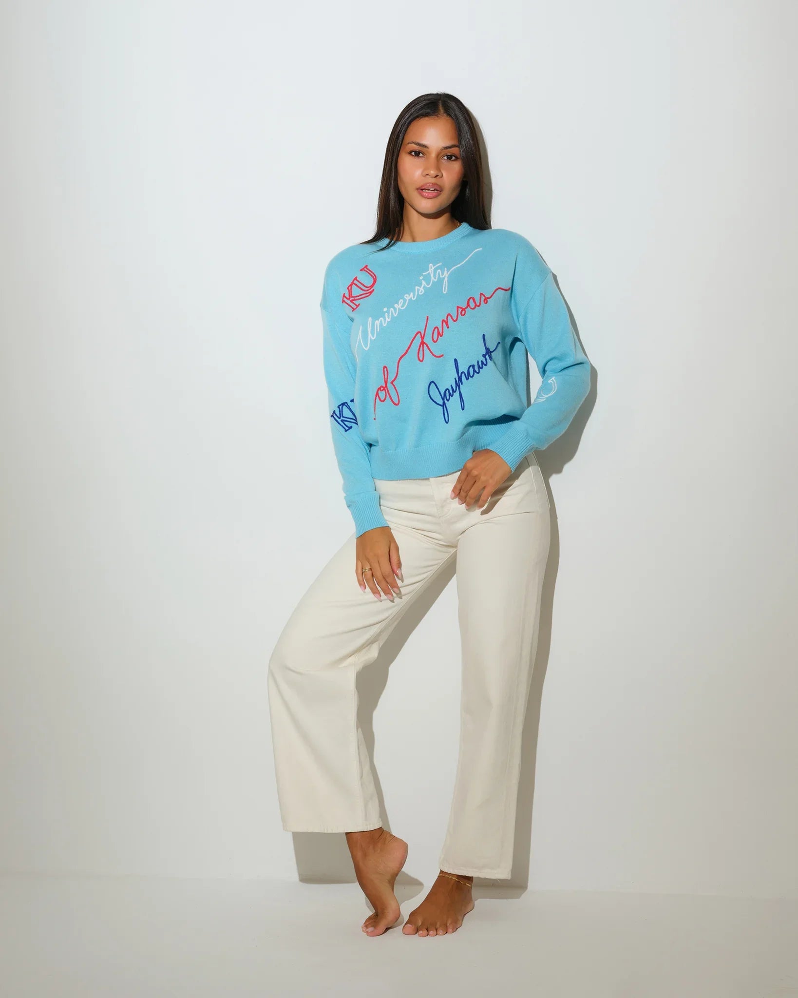 Powder blue Kansas Jayhawks crewneck sweater with cursive "University of Kansas Jayhawks" script and KU logo embroidery in red and blue.