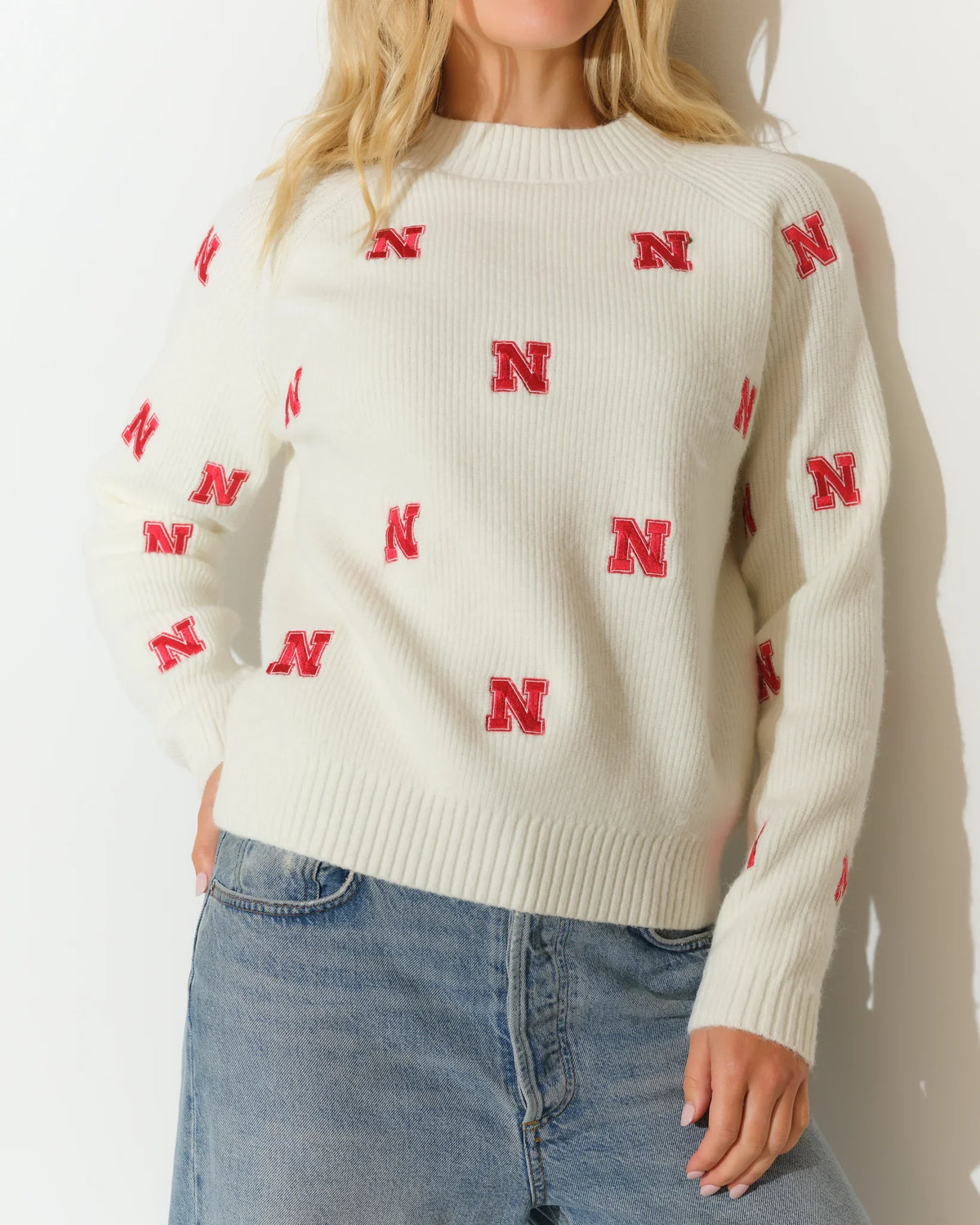 Ivory Nebraska Cornhuskers fisherman sweater with allover red "N" logo pattern, crew neck, and long sleeves, styled with jeans.