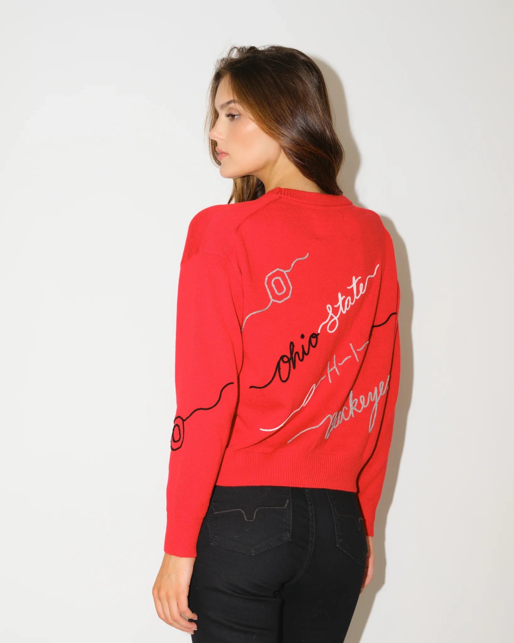 Red Ohio State Buckeyes long-sleeve sweater with cursive script lettering across the chest, styled with black flare pants.