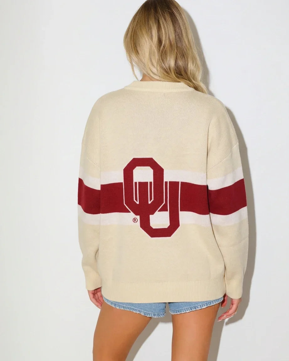 Cream Oklahoma Sooners oversized cardigan with crimson and white chest stripes, gold buttons, a helmet patch, and "Boomer Sooner" lettering on the front pocket.