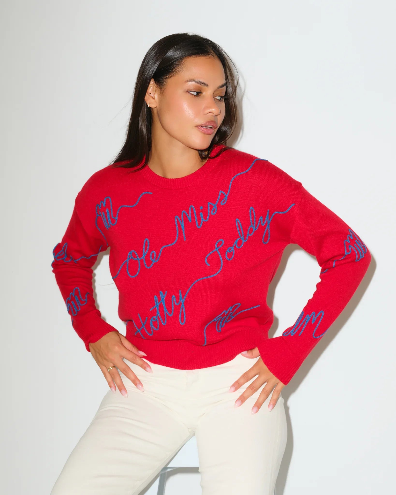 Red Ole Miss Rebels crewneck sweater featuring allover blue cursive "Ole Miss Rebels" script lettering, styled with white pants.