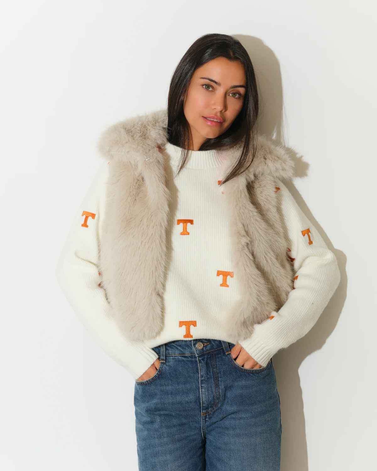Ivory Tennessee Volunteers faux fur vest with hood, worn over a white knit sweater featuring orange "T" logos, paired with jeans.