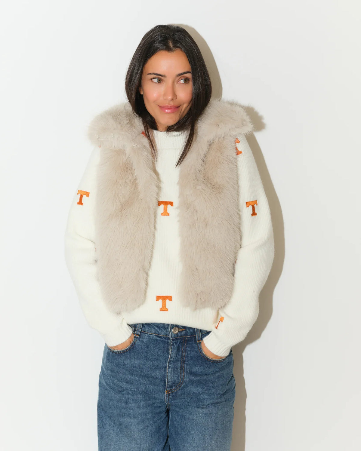 Ivory Tennessee Volunteers faux fur vest with hood, worn over a white knit sweater featuring orange "T" logos, paired with jeans.