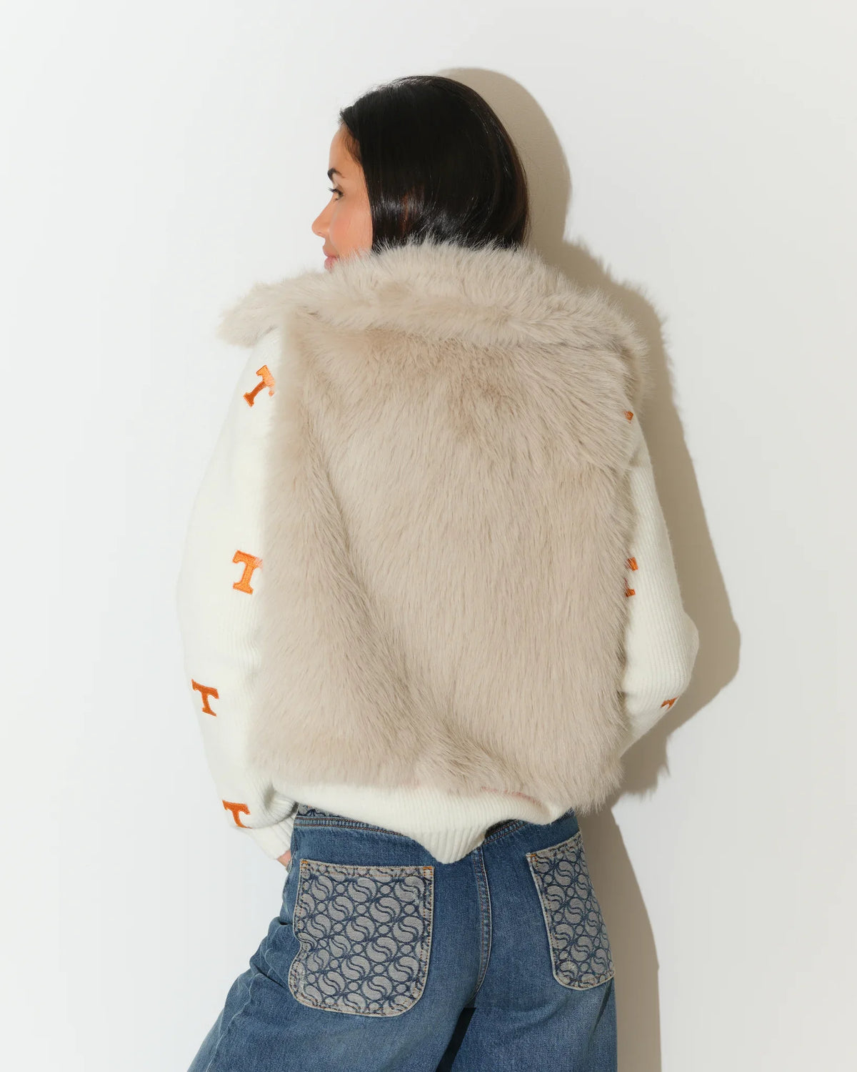 Ivory Tennessee Volunteers faux fur vest with hood, worn over a white knit sweater featuring orange "T" logos, paired with jeans.