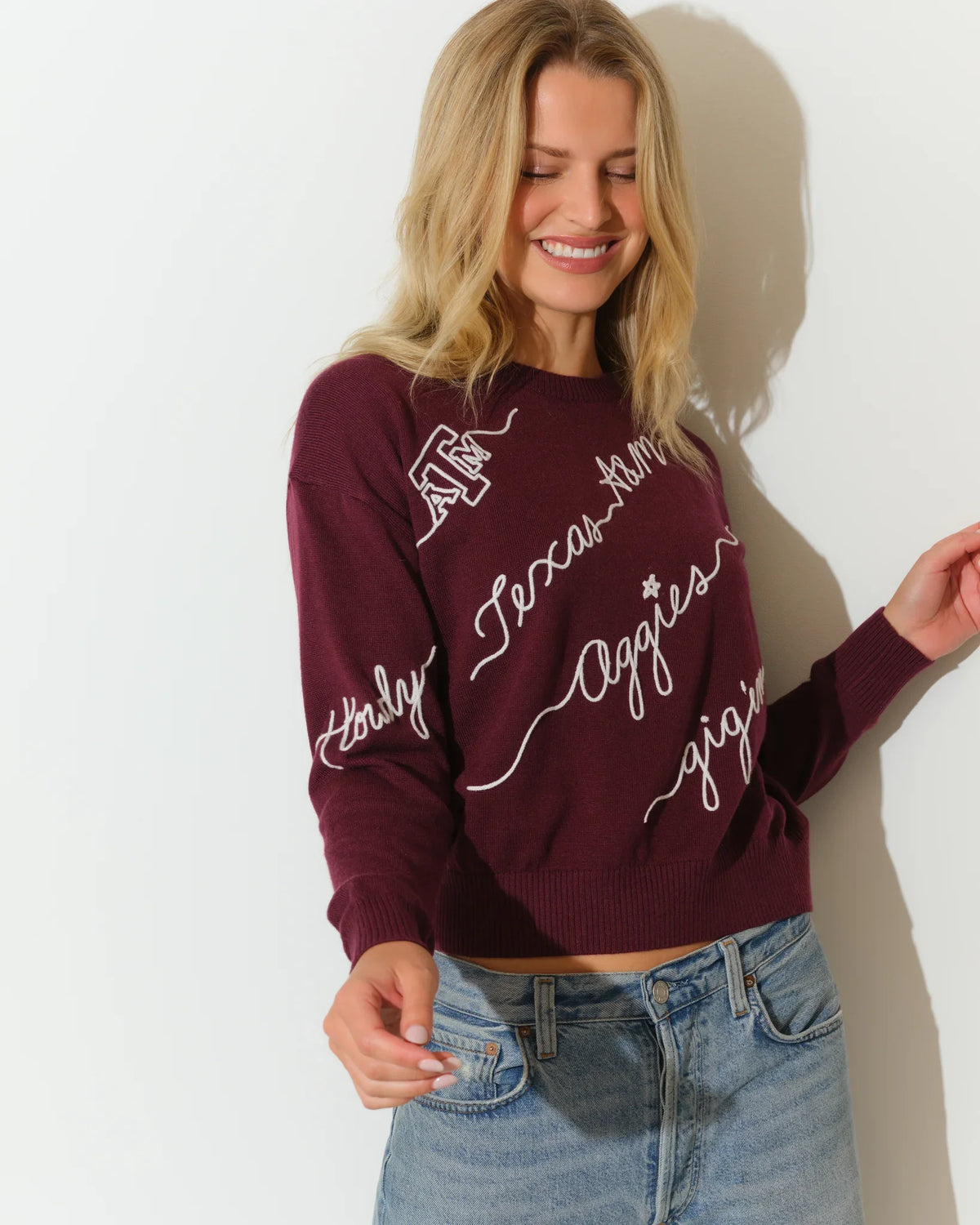 Maroon Texas A&M Aggies cropped crewneck sweater with white cursive script lettering across the front, paired with light wash jeans.