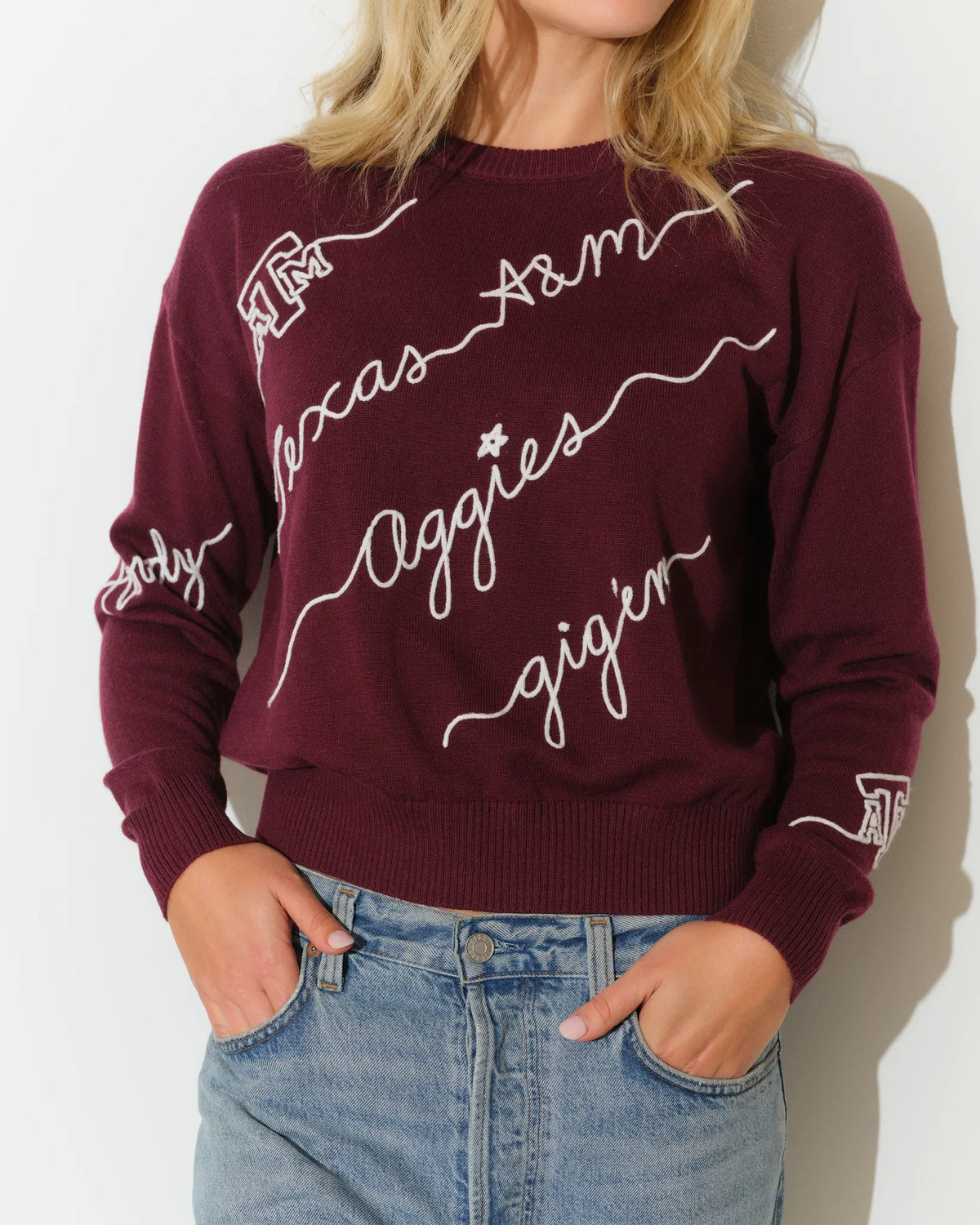 Maroon Texas A&M Aggies cropped crewneck sweater with white cursive script lettering across the front, paired with light wash jeans.