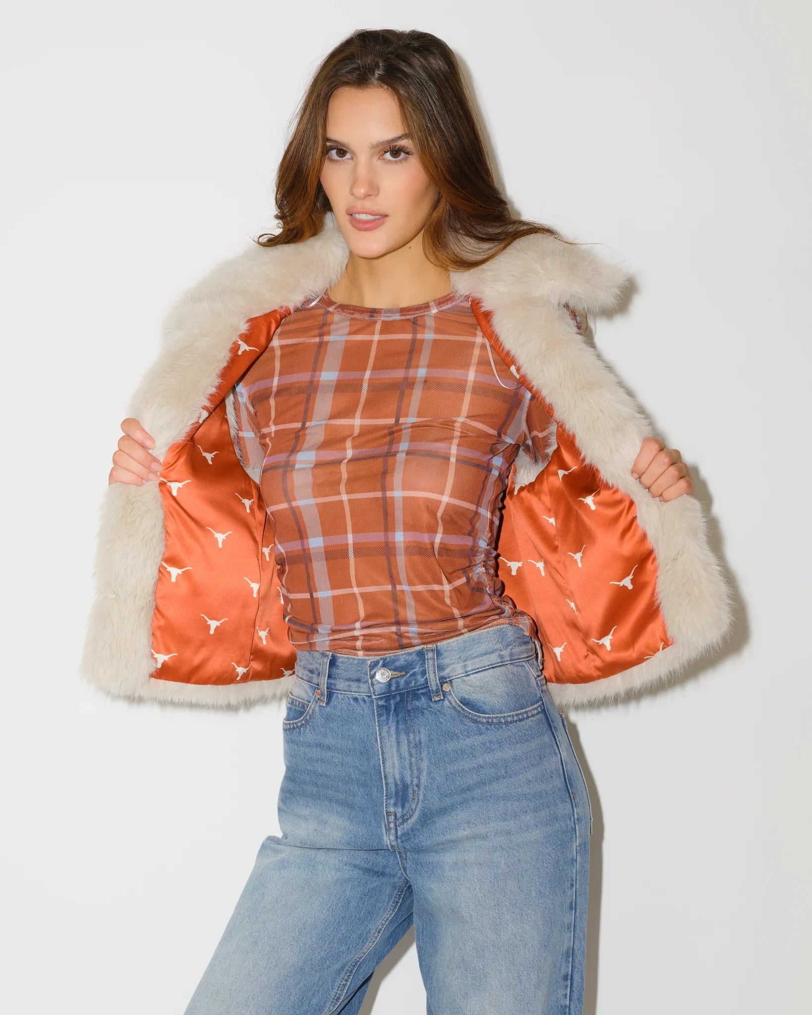 Ivory faux fur Texas Longhorns vest shown open, revealing an orange plaid lining with Longhorns logo print, paired with jeans.