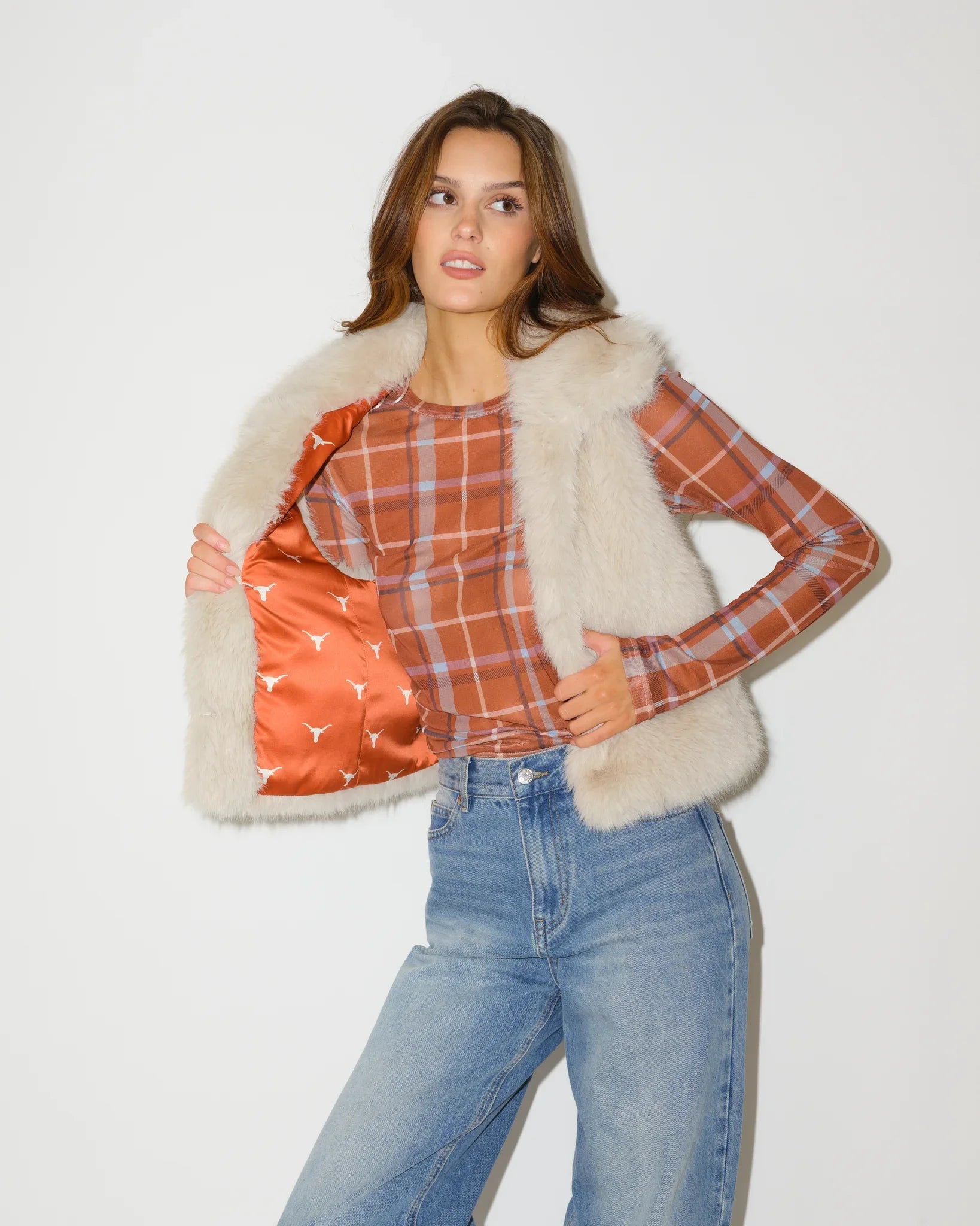 Ivory faux fur Texas Longhorns vest shown open, revealing an orange plaid lining with Longhorns logo print, paired with jeans.