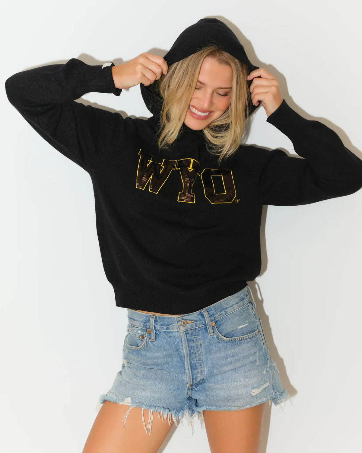 Black Wyoming Cowboys sequin knit hoodie featuring gold sequin "WYO" lettering on the chest, modeled with a relaxed fit.