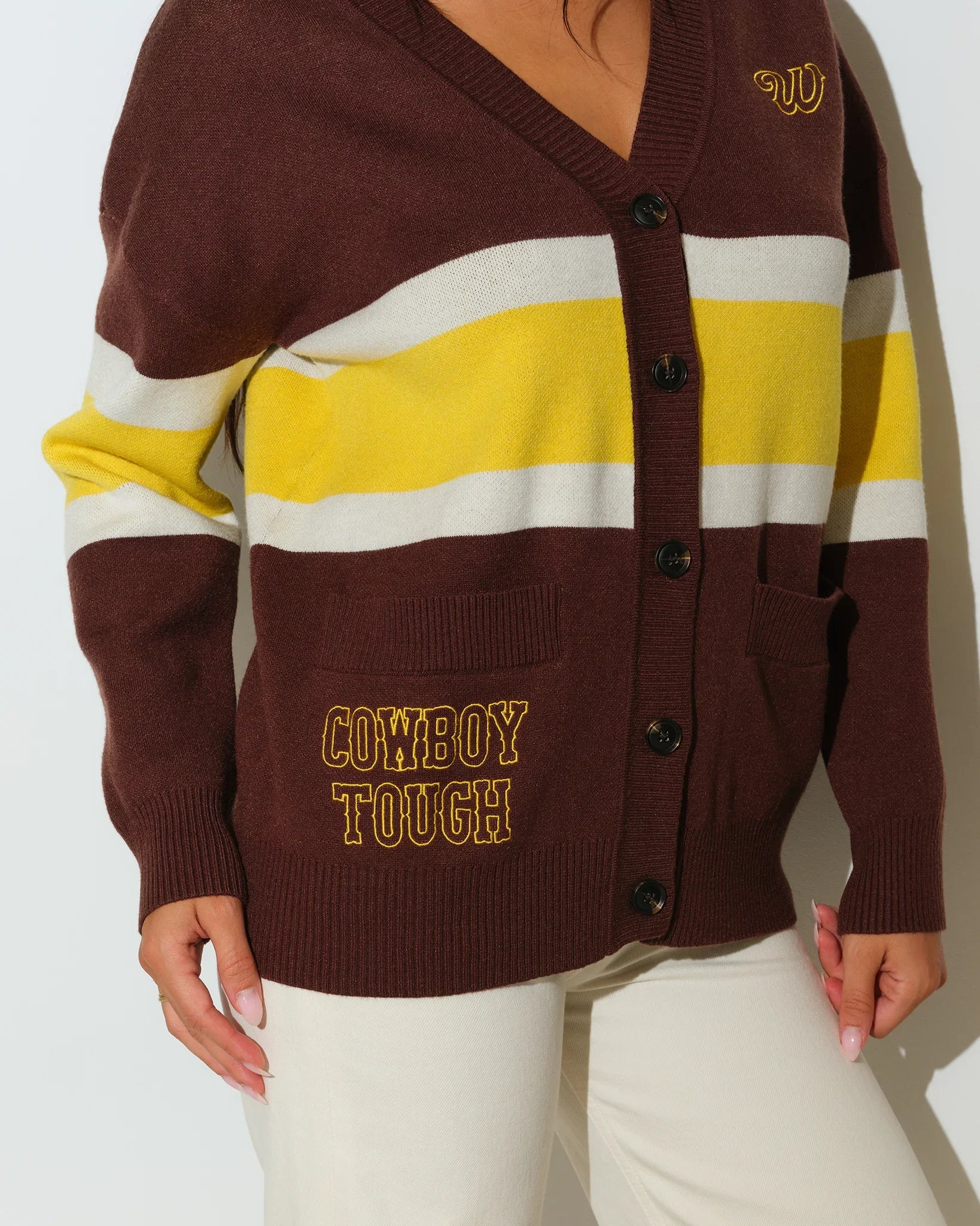 Brown Wyoming Cowboys oversized cardigan with yellow and white chest stripes, gold embroidered logo, and "Wyoming Cowboys" text on the hem.