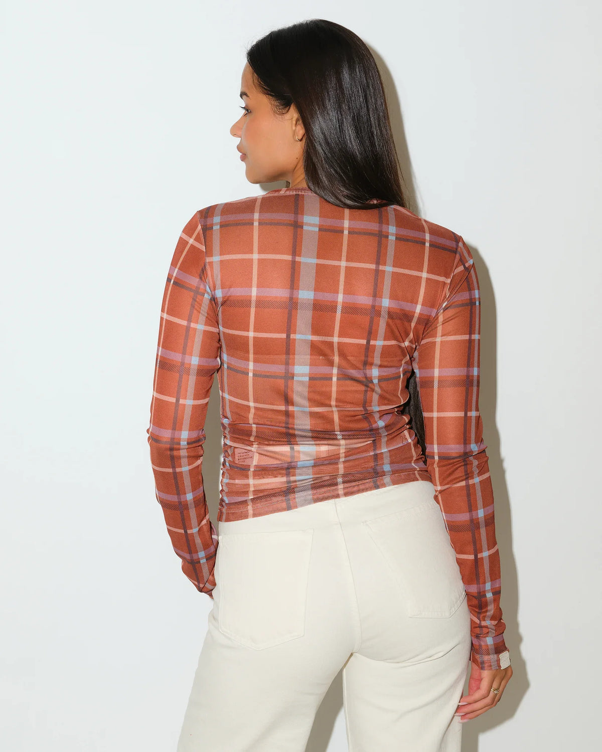 Brown plaid KadyLuxe mesh long sleeve top with a crew neckline and sheer overlay, styled with white pants.