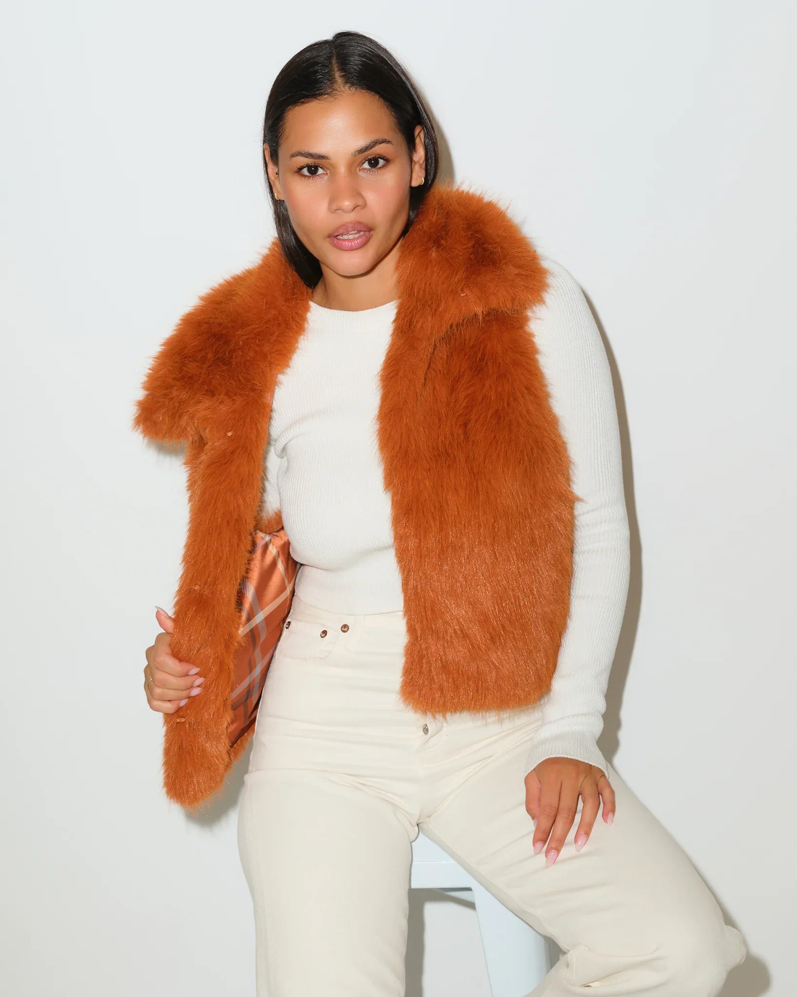 Saddle brown KADYLUXE faux fur vest with plaid lining, worn open over a white top with cream pants.
