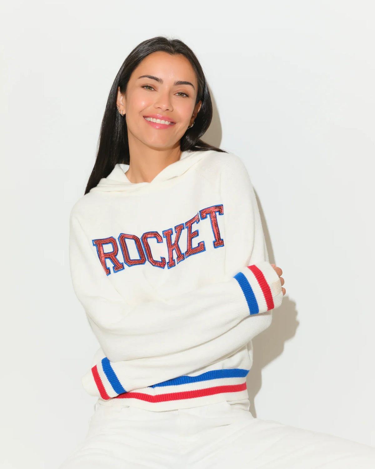 White KADYLUXE Shine Sequin Knit Hoodie with "ROCKET" in red-blue sequin letters, red and blue stripe cuffs and hem.