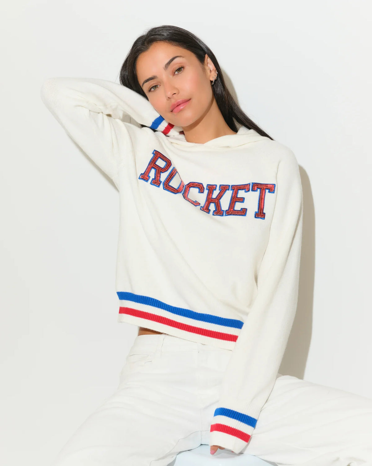 White KADYLUXE Shine Sequin Knit Hoodie with "ROCKET" in red-blue sequin letters, red and blue stripe cuffs and hem.
