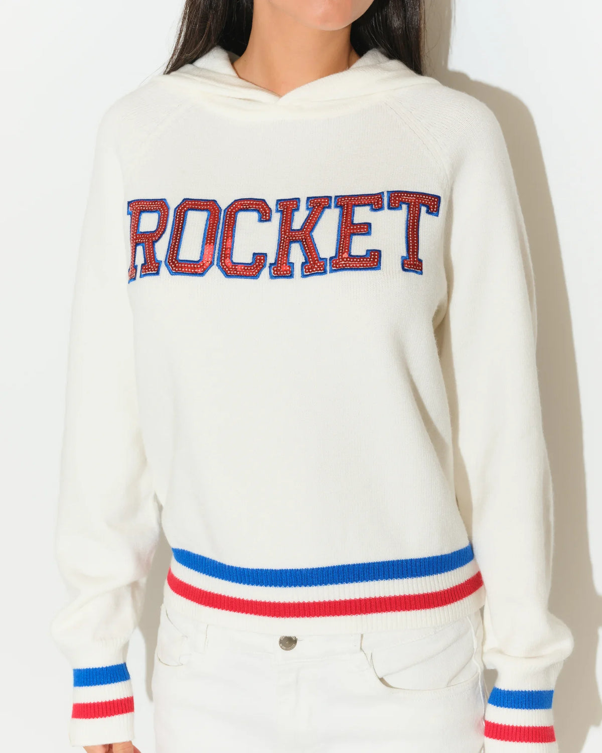 White KADYLUXE Shine Sequin Knit Hoodie with "ROCKET" in red-blue sequin letters, red and blue stripe cuffs and hem.