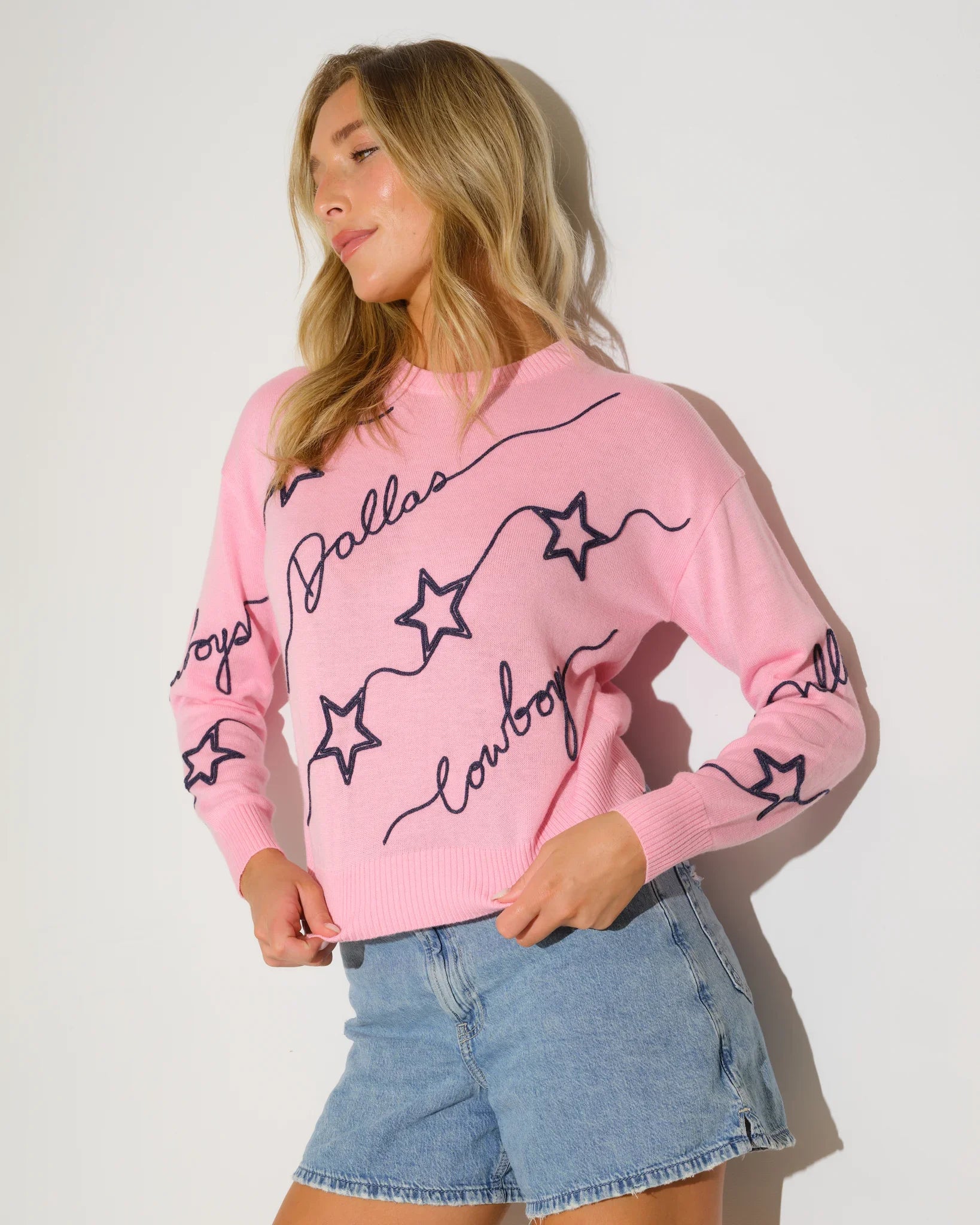 Pink Dallas Cowboys women's knit sweater with navy star pattern and script "Dallas Cowboys" lettering throughout the fabric.