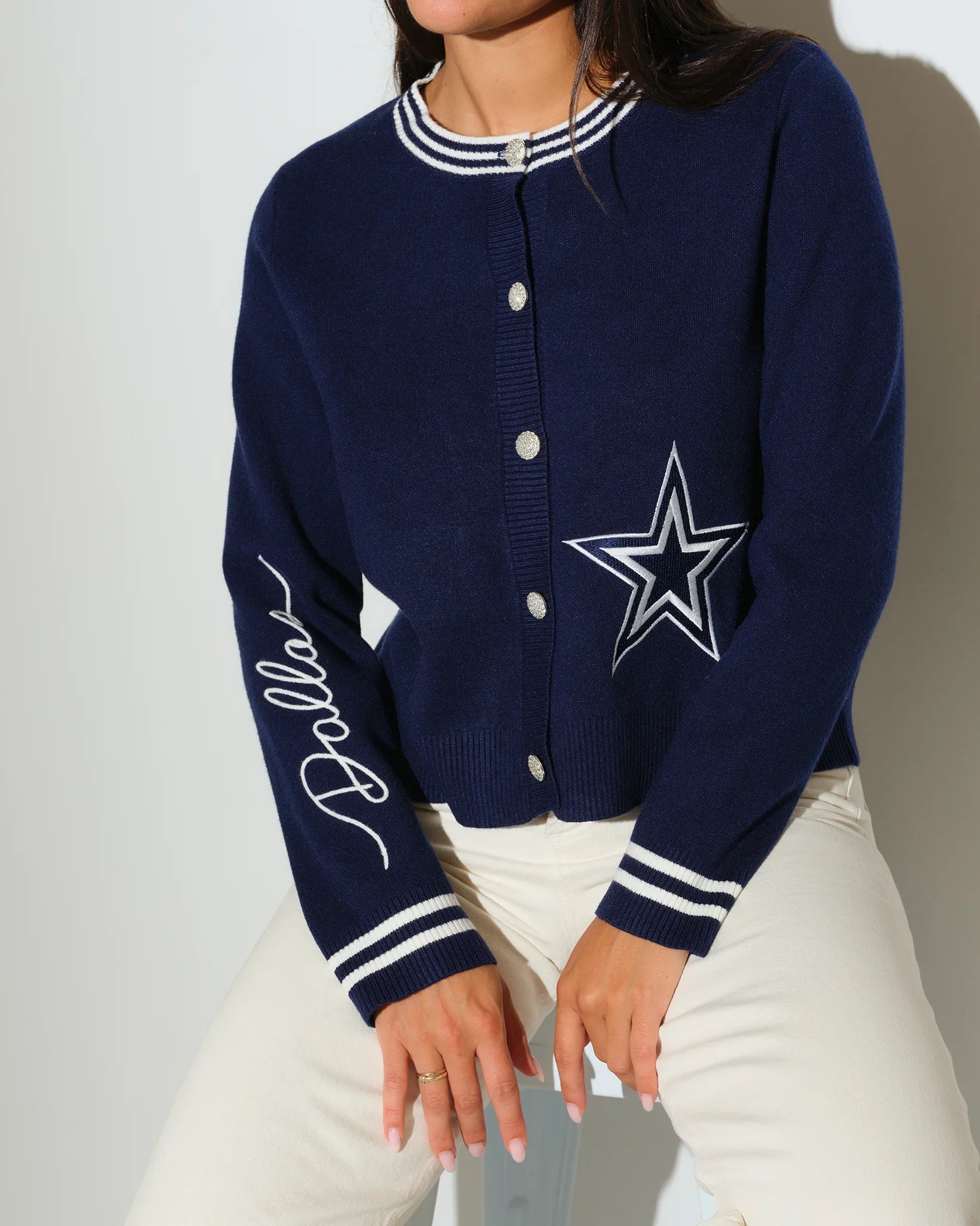Navy Dallas Cowboys mini cardigan with silver star logo on chest, striped trim, and "Cowboys" script on sleeve, styled on a seated female model.